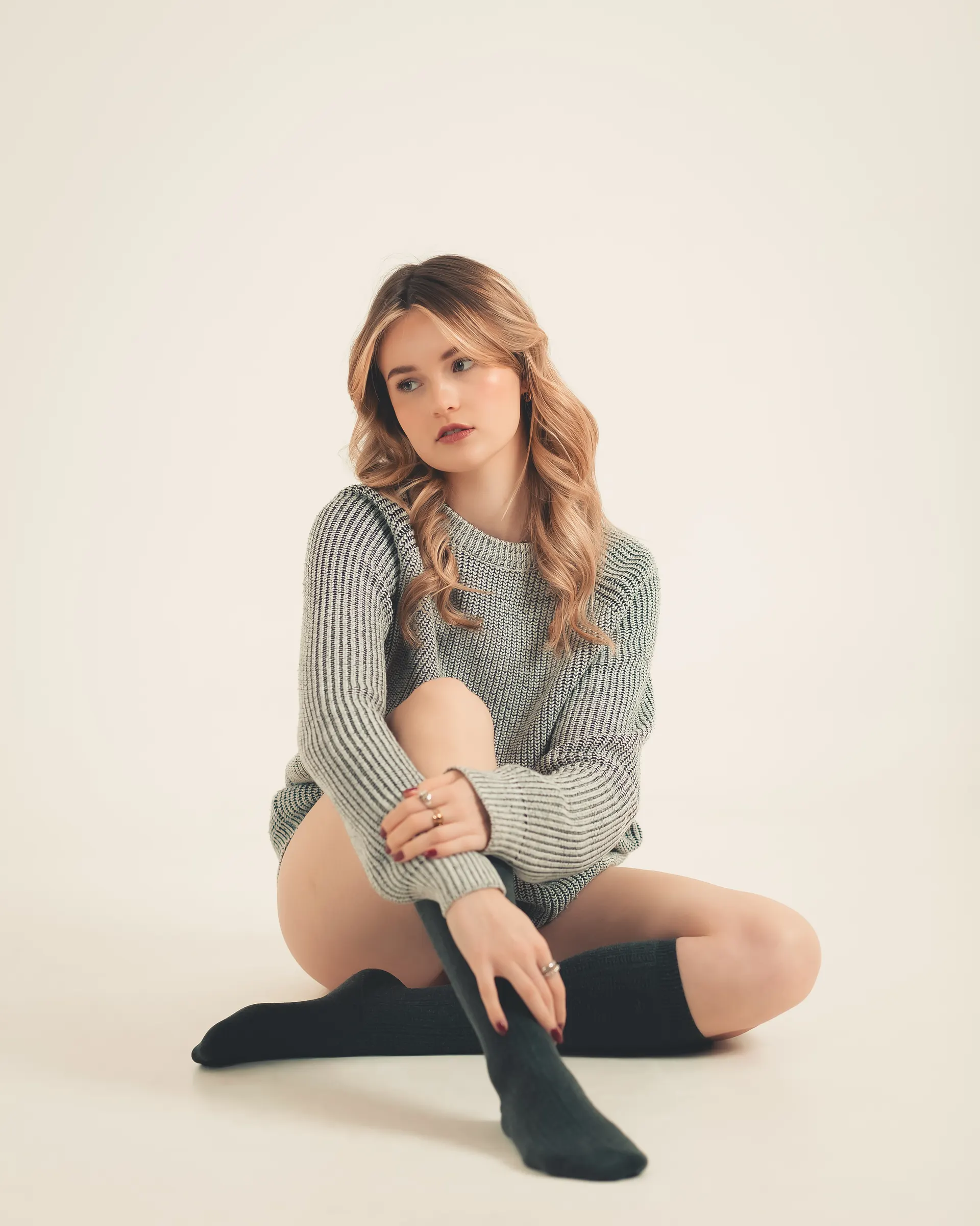Studio portrait seated on the floor in a knit sweater.
